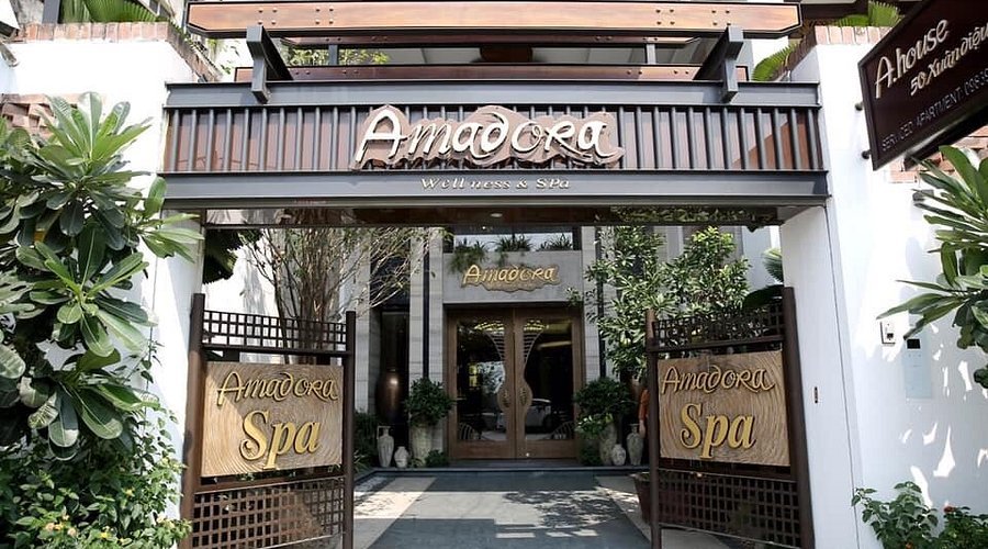 Lối vào spa với cổng gỗ, cây xanh hai bên và biển hiệu "Amadora Spa".
