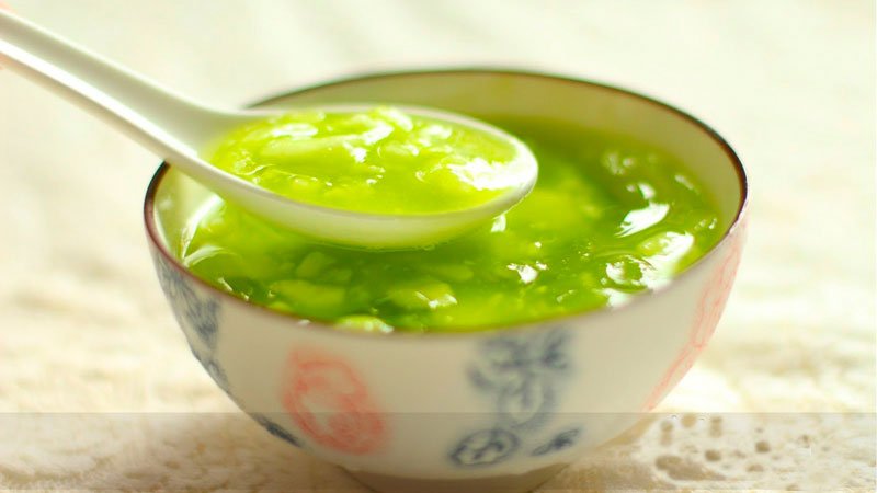 Chén chè đậu xanh với nước cốt dừa màu xanh lá, với muỗng sứ trắng đặt trên mặt chè.