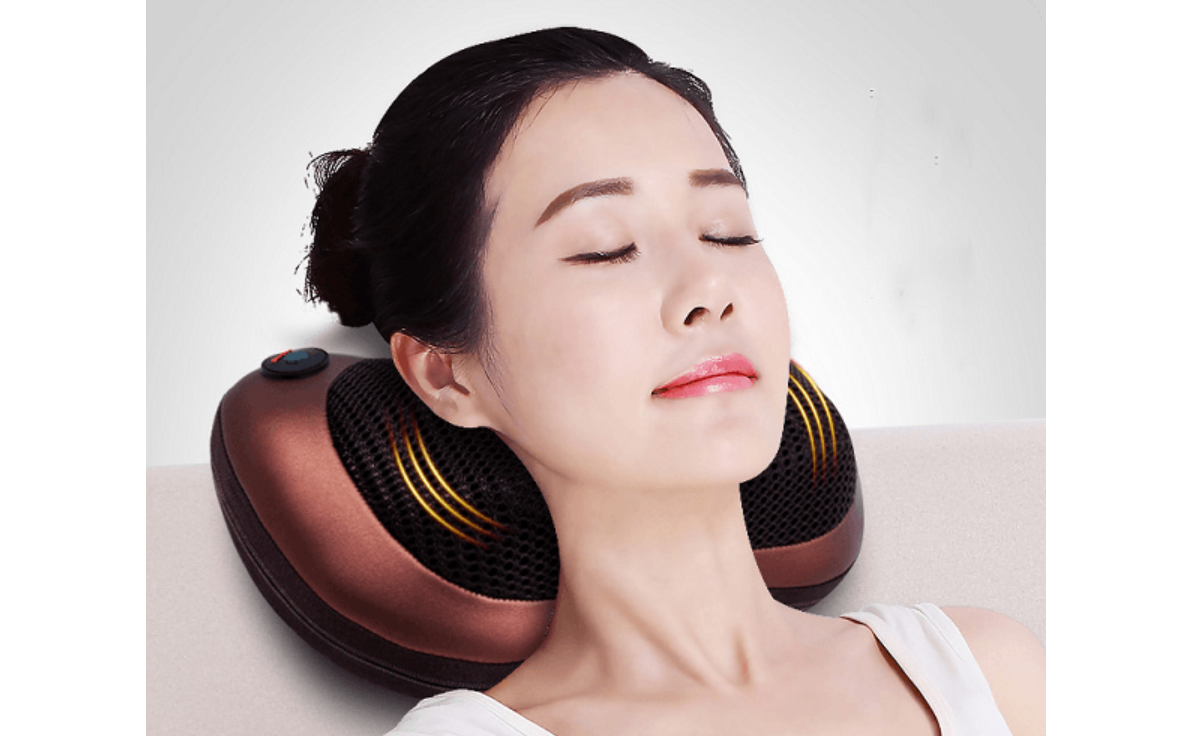 Người phụ nữ thư giãn với gối massage cổ màu nâu, mắt nhắm, tựa trên ghế sáng màu.