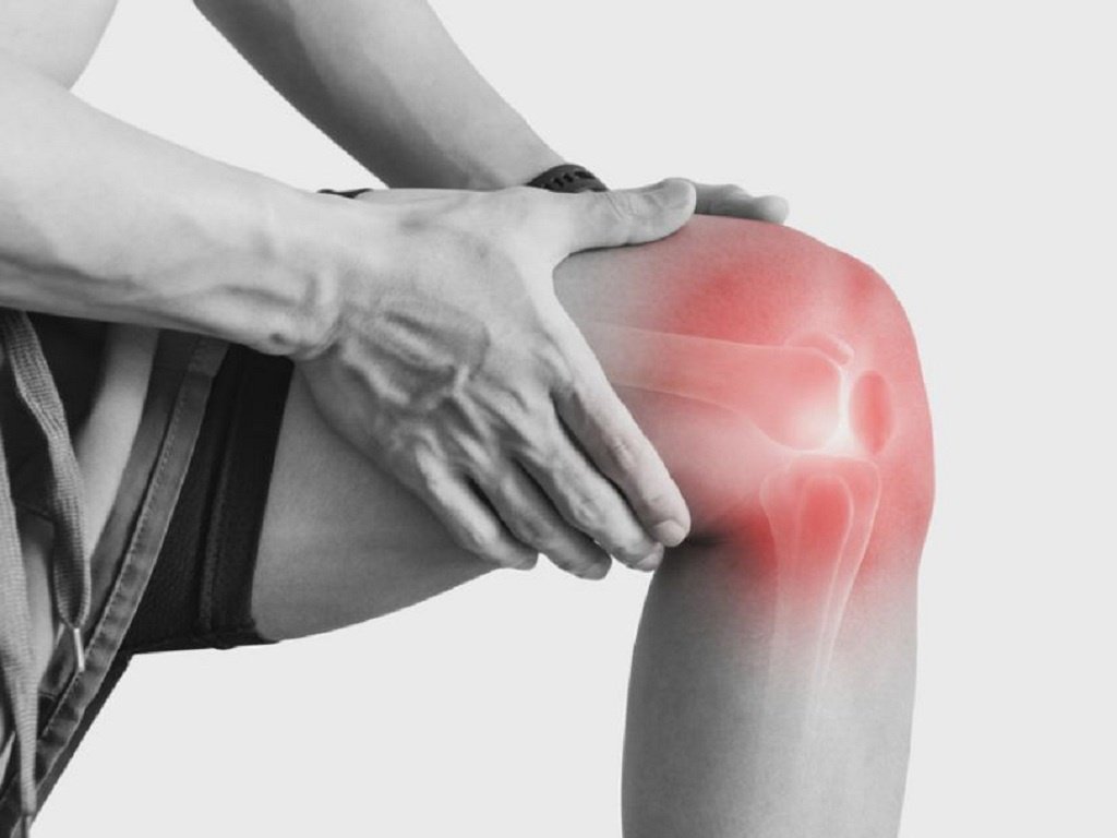 Người đang chạm vào đầu gối bị đau, với phần khớp gối được làm nổi bật bằng màu đỏ.