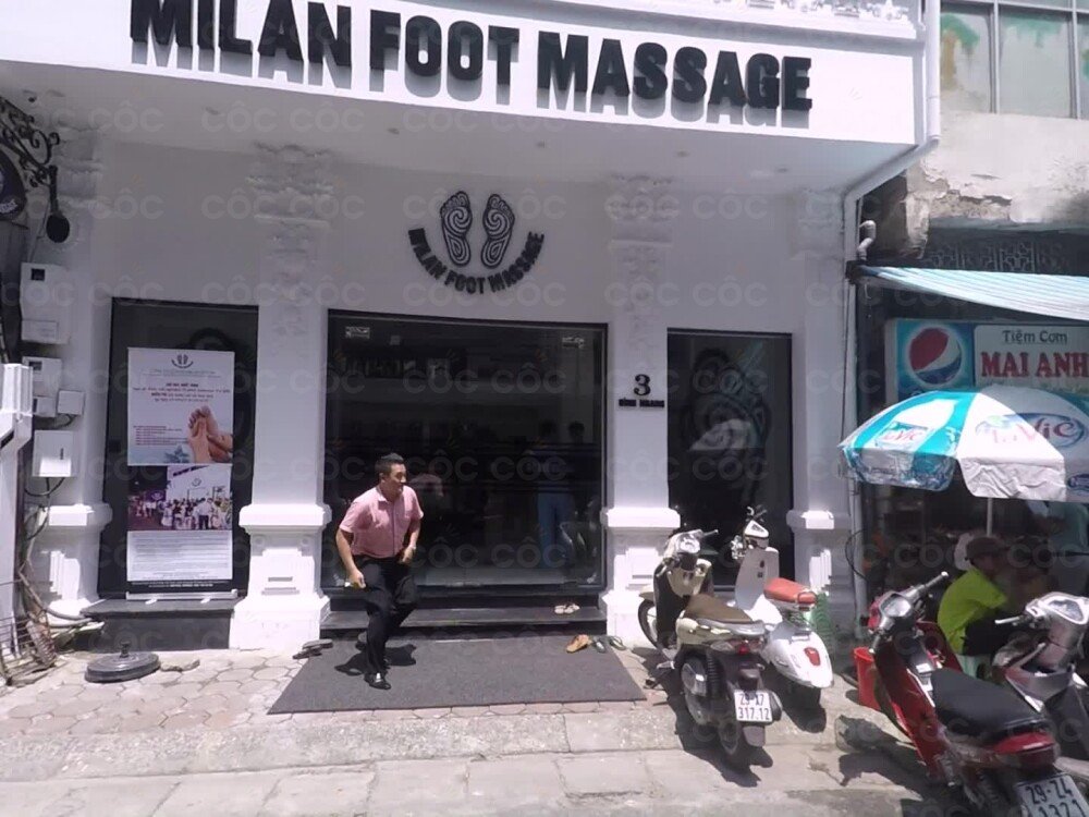 Mặt tiền tiệm massage chân với bảng hiệu lớn và xe máy đỗ phía trước.