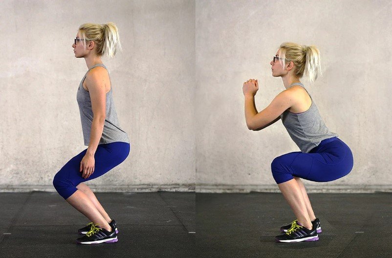 Người đang thực hiện động tác squat trong phòng tập, mặc áo ba lỗ và quần tập, mang giày thể thao.