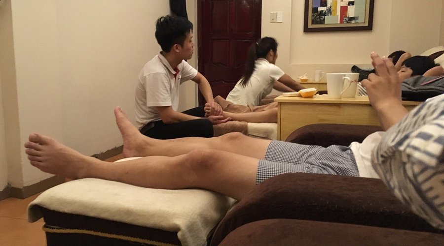 Một nhóm người đang thư giãn và mát-xa chân trong một căn phòng có ghế dài và bàn nhỏ.