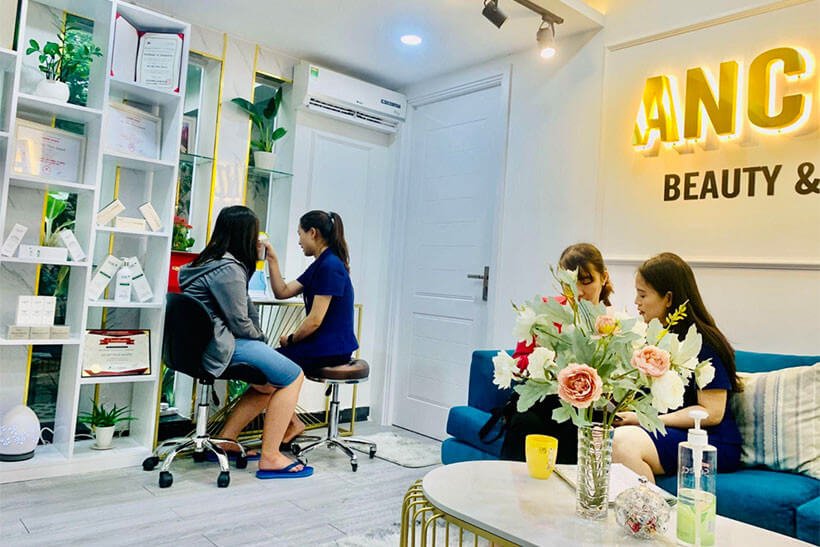 Hai người đang trò chuyện trong tiệm làm đẹp, xung quanh là cây và đồ trang trí nội thất.