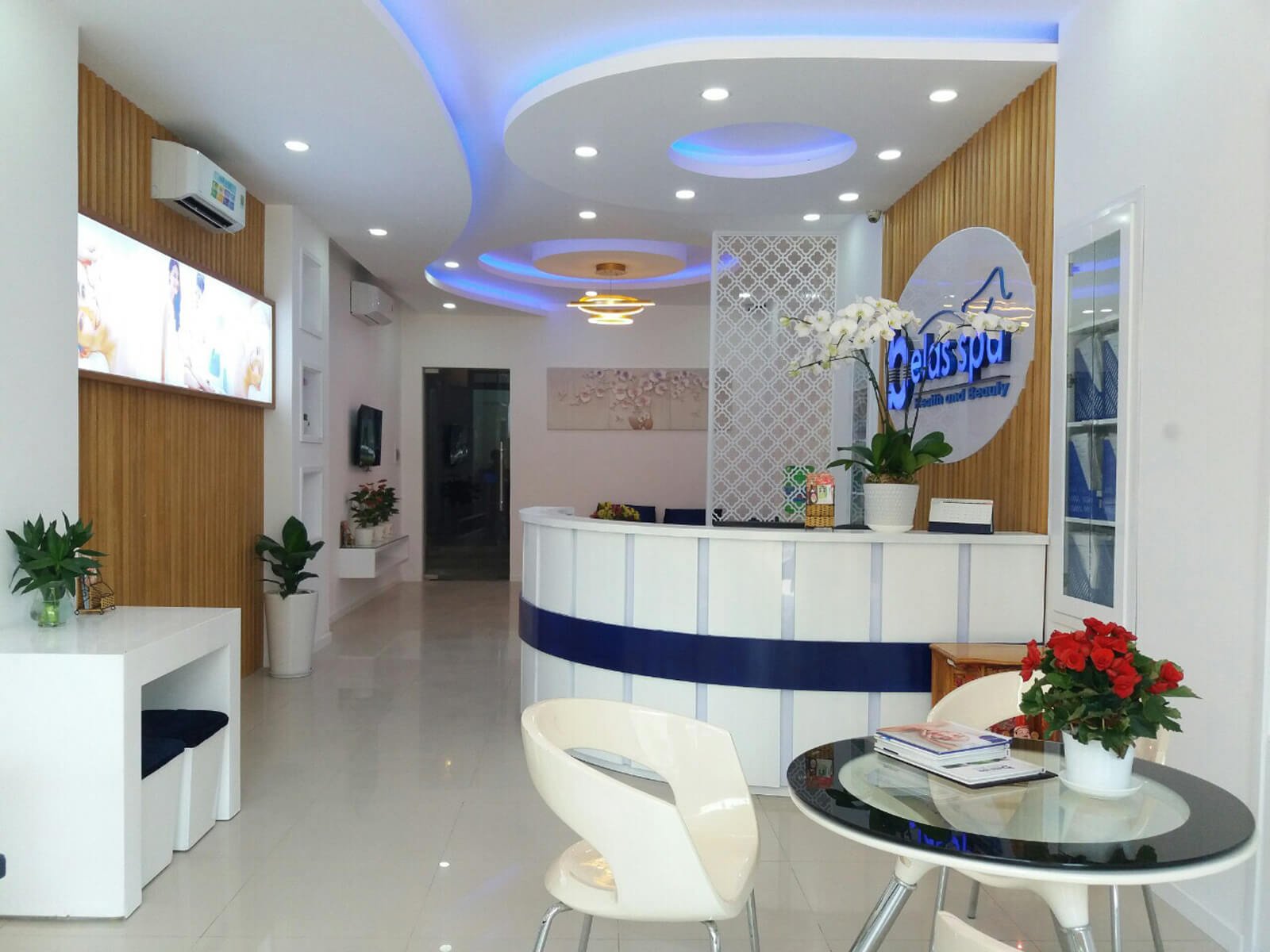 Nội thất spa với quầy lễ tân, bàn ghế hiện đại và cây xanh trang trí, tạo không gian thư giãn.