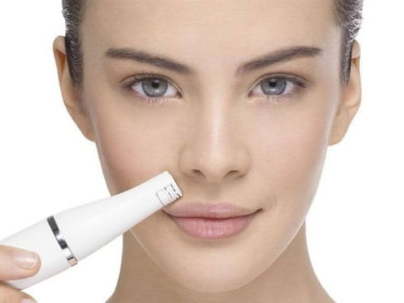 Người đang sử dụng thiết bị làm đẹp da mặt, tập trung vào vùng mũi và miệng, nền trắng.
