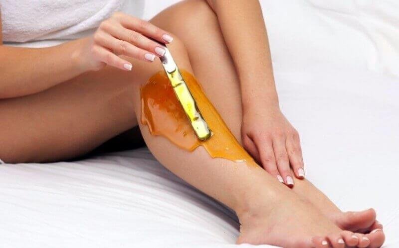 Người dùng thoa sáp ong lên chân bằng một thanh gỗ nhỏ trên nền giường trắng.