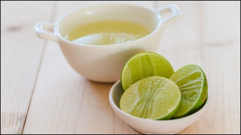 Chén nước chanh tươi và đĩa nhỏ đựng chanh cắt đôi, đặt trên bàn gỗ sáng màu.