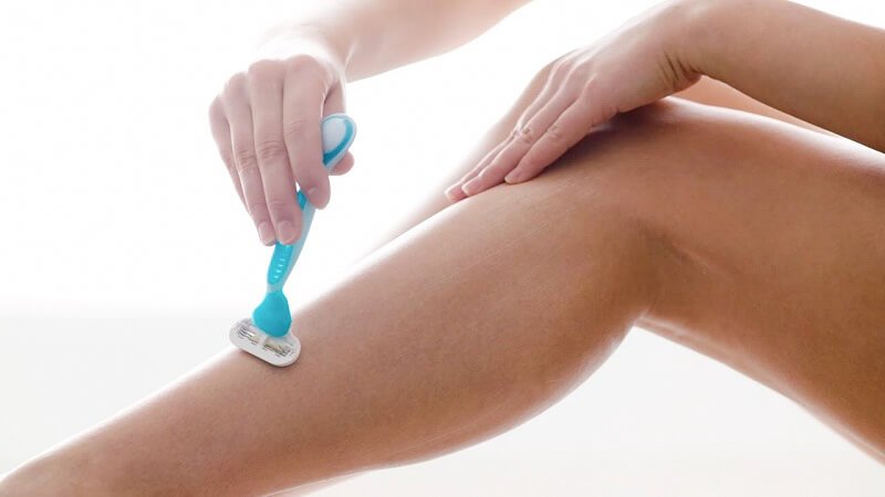 Người đang sử dụng dao cạo màu xanh cạo lông trên chân trần trong không gian sáng.