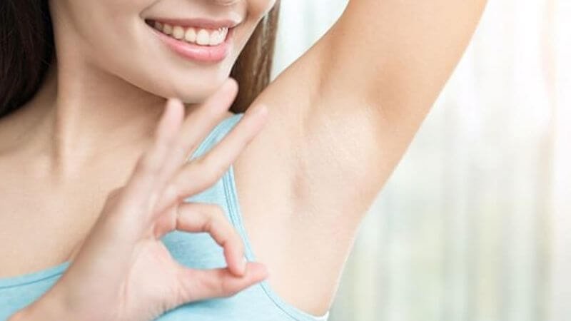 Người mặc áo xanh mỉm cười, giơ tay, tạo dáng với ký hiệu OK, nhấn mạnh vùng da dưới cánh tay.