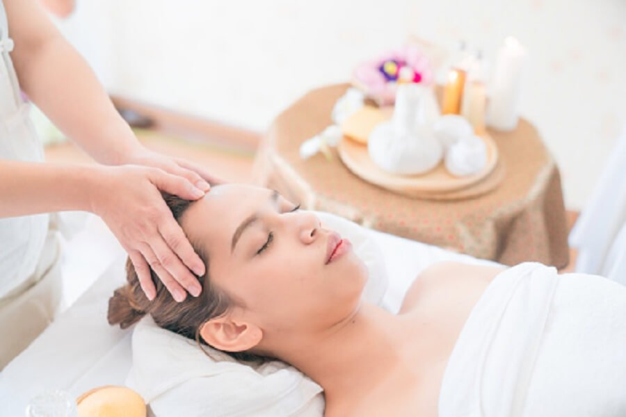 Người nằm thư giãn trong phòng spa, được massage đầu, xung quanh có nến và vật dụng trang trí.