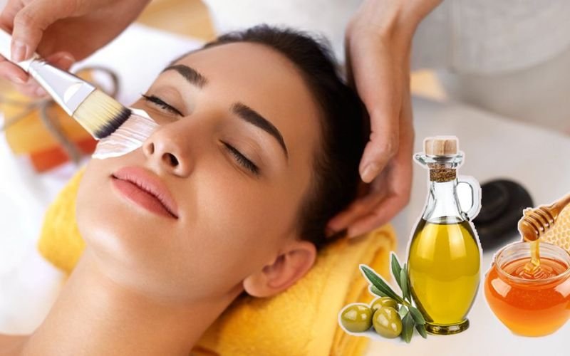 Người đang đắp mặt nạ dưỡng da, bên cạnh là hình ảnh chai dầu ô liu và mật ong.