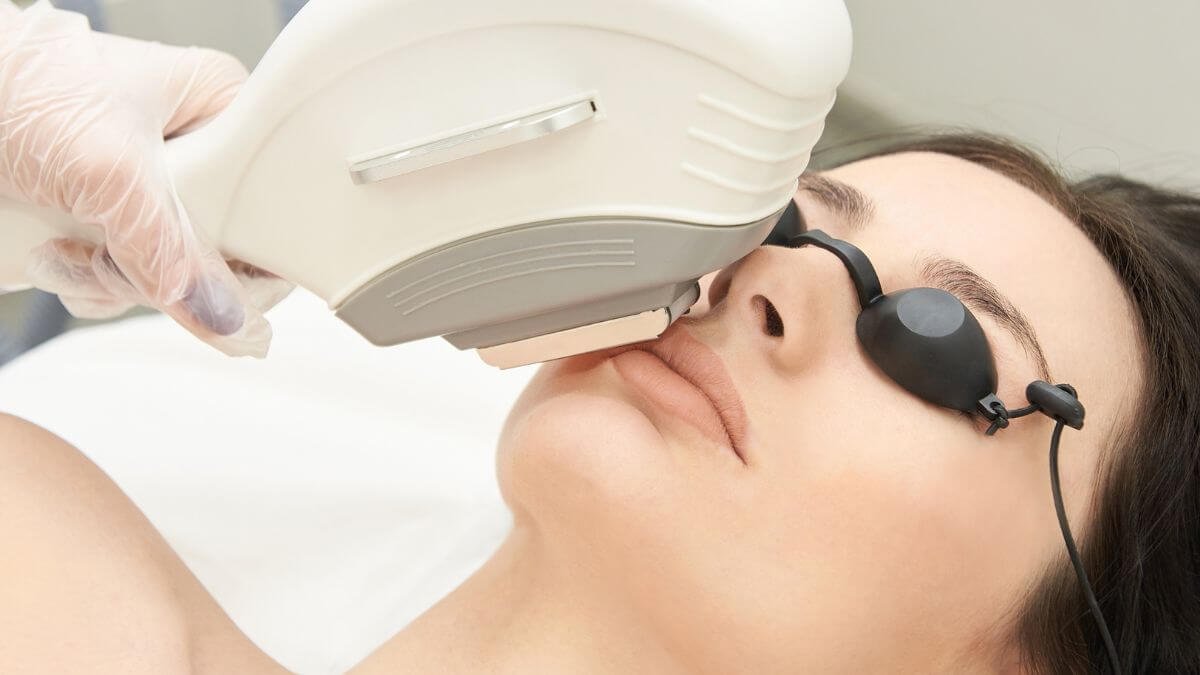 Người đeo kính bảo vệ đang được trị liệu bằng máy laser trên mặt trong môi trường y tế.