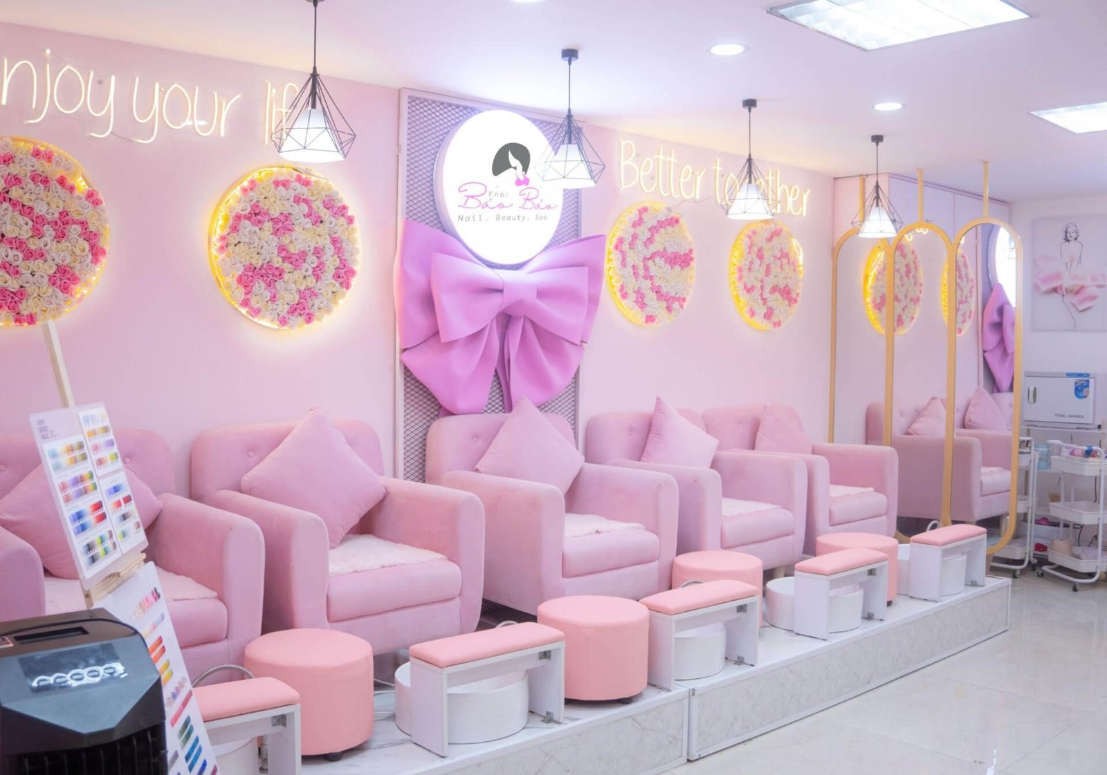 Nội thất tiệm spa với ghế màu hồng, trang trí hoa và đèn neon, tạo không gian thư giãn và thẩm mỹ.