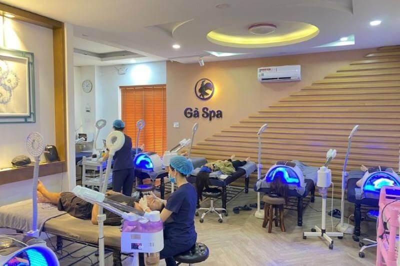 Phòng spa với giường trị liệu, thiết bị chăm sóc da, và nhân viên đang làm việc, không gian hiện đại và thoải mái.