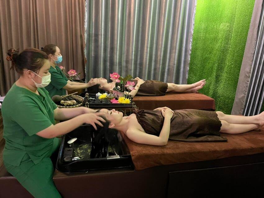 Nhân viên spa chăm sóc tóc và da mặt cho khách trong không gian thư giãn với hoa trang trí.