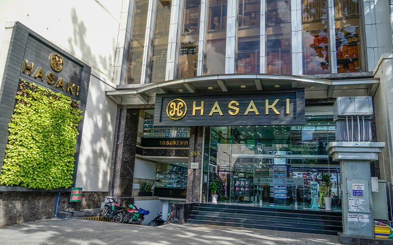 Mặt tiền một cửa hàng có bảng hiệu "HASAKI", với cửa kính lớn và xe máy đỗ phía trước.