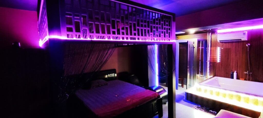 Phòng ngủ với giường có rèm trang trí, ánh sáng tím, có bồn tắm lớn và máy điều hòa không khí trên tường.