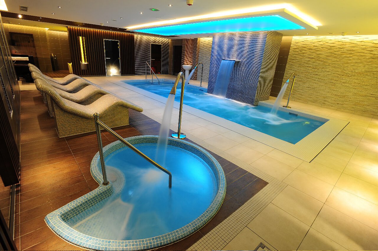 Khu vực spa hiện đại với hồ bơi, ghế thư giãn và thác nước trong không gian nội thất sang trọng.