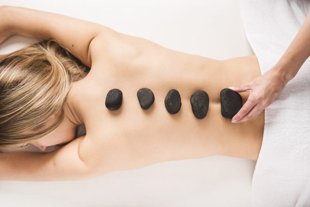 Người đang nằm thư giãn, có năm viên đá nóng đặt dọc trên lưng trong liệu pháp massage.