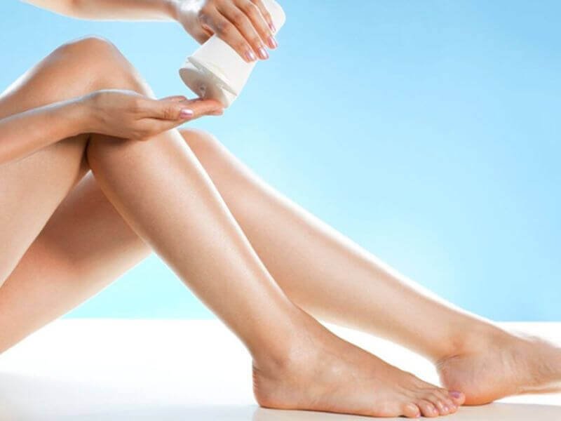 Người đang thoa kem dưỡng lên tay với đôi chân đặt trên nền xanh nhạt.