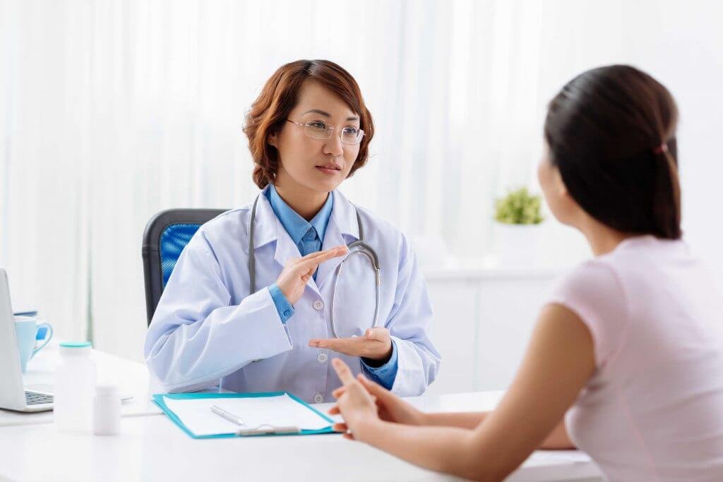 Bác sĩ trò chuyện với bệnh nhân trong văn phòng, có tài liệu và chai lọ trên bàn.