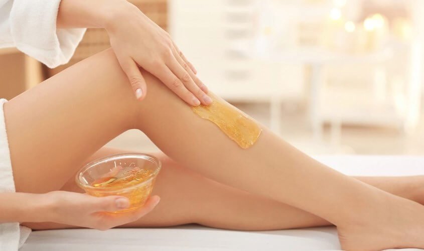 Người đang thoa sáp lên chân, chuẩn bị cho quá trình tẩy lông, trong không gian spa thư giãn.