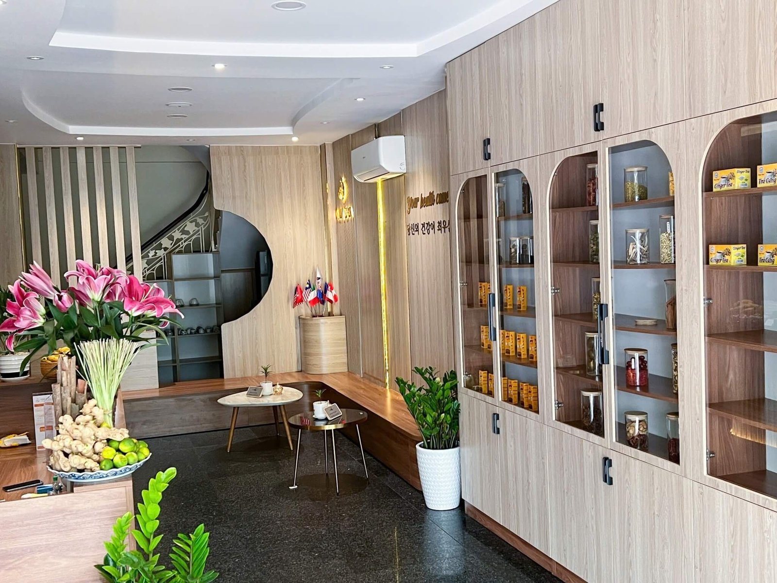 Căn phòng với kệ gỗ trưng bày sản phẩm, bàn nhỏ, bình hoa và cây xanh trang trí.