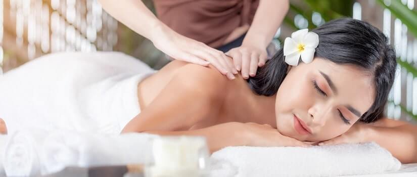 Người phụ nữ nằm thư giãn trên bàn massage, có hoa trên tóc, được xoa bóp lưng trong không gian spa thư giãn.