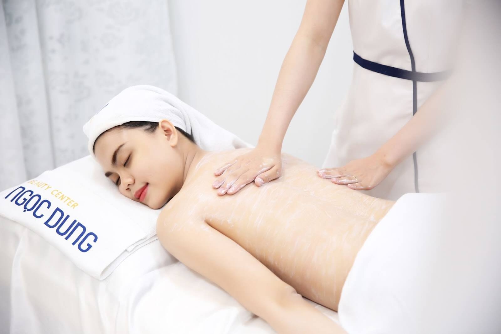Người đang nhận dịch vụ massage thư giãn tại spa, nằm úp trên giường, khăn quấn đầu trắng.