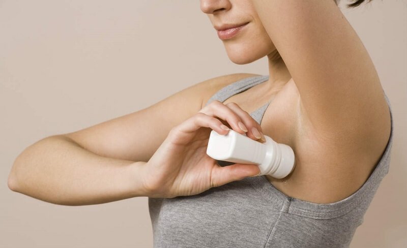 Người đang sử dụng lăn khử mùi dưới cánh tay, mặc áo không tay màu xám.