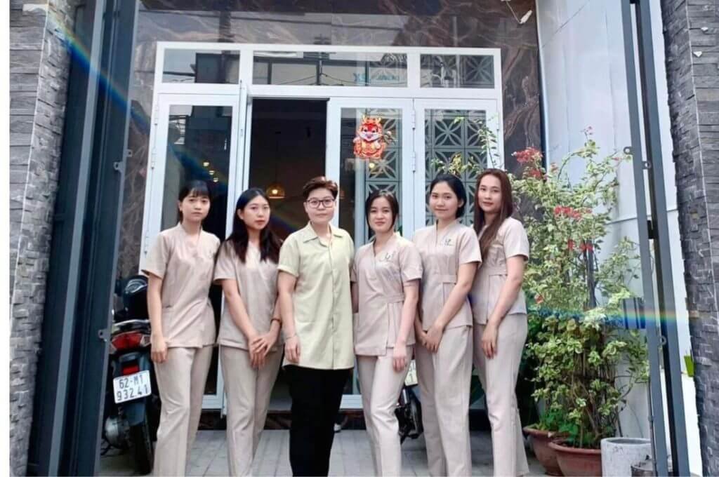 Một nhóm người mặc đồng phục đứng trước cửa một tòa nhà với cây cảnh xung quanh.