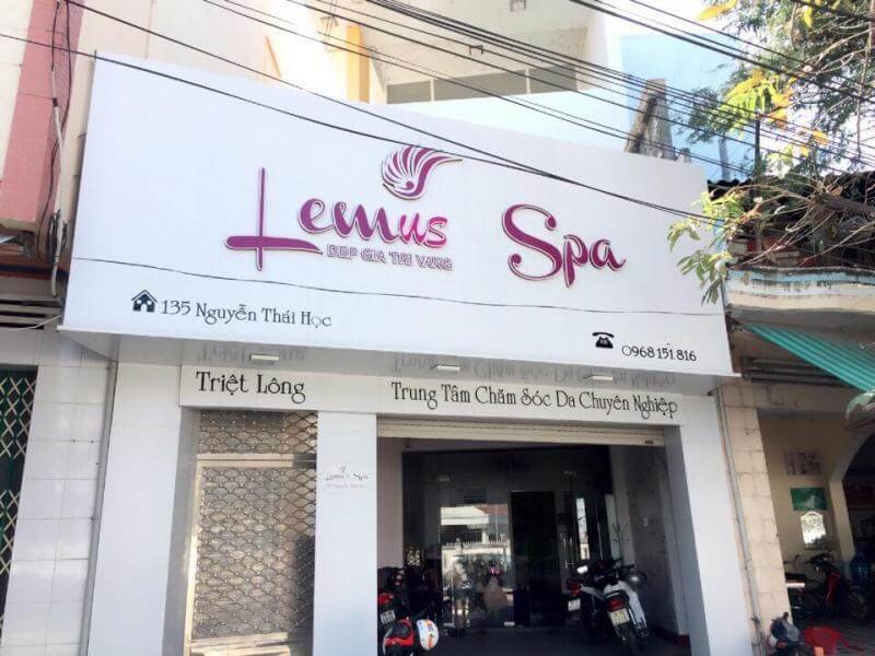Mặt tiền một spa với bảng hiệu màu trắng và chữ màu hồng, bên ngoài có xe máy đỗ.