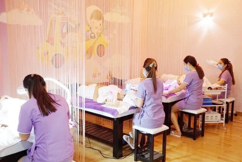 Nhân viên mặc đồng phục tím đang chăm sóc khách hàng trong spa với trang trí tường màu sắc.