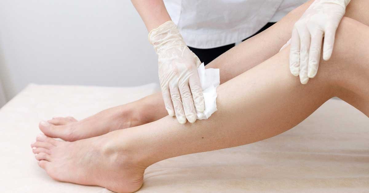 Người đeo găng tay đang thực hiện chăm sóc da chân bằng bông lau trên bề mặt phẳng.