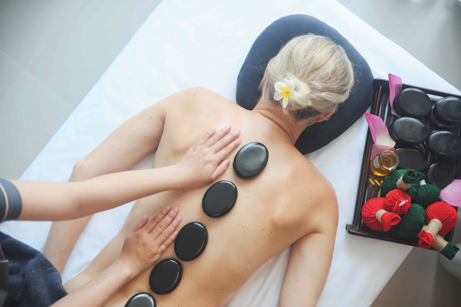 Người nằm úp mặt trên giường massage, lưng được đặt đá nóng, bên cạnh là khay đựng dầu và dụng cụ spa.