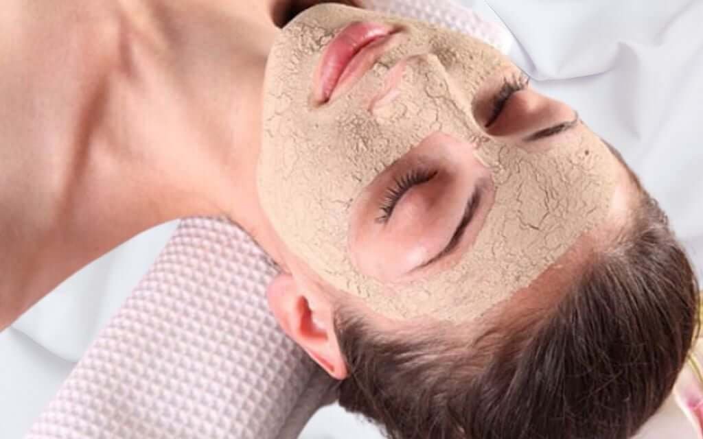 Người đang thư giãn trên giường với mặt nạ dưỡng da màu sáng trên khuôn mặt.