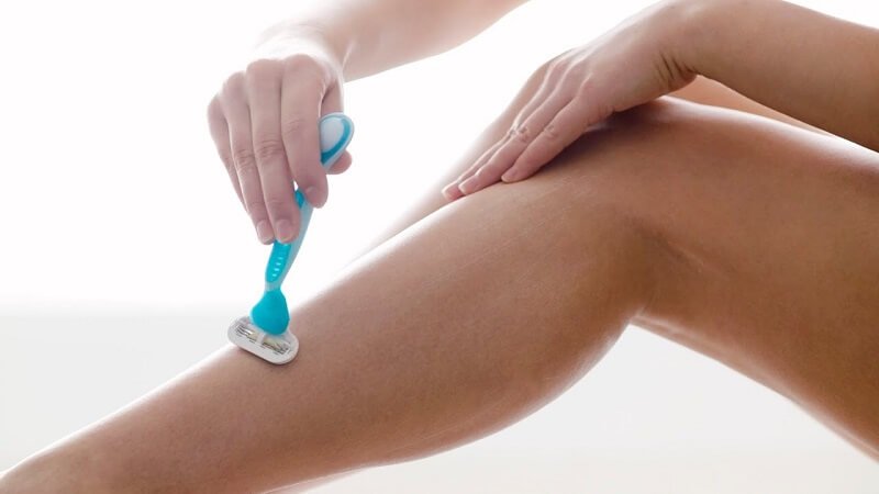 Người đang cạo lông chân bằng dao cạo màu xanh trên nền trắng.