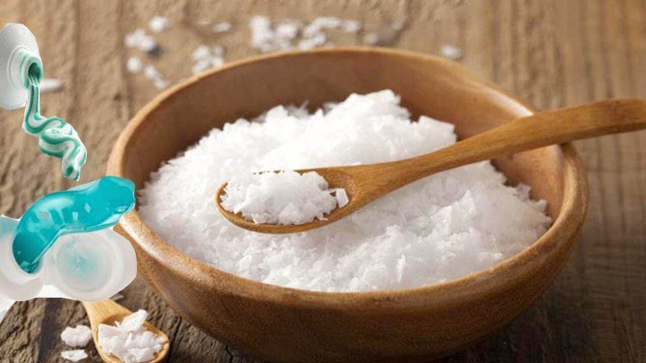 Bát gỗ chứa muối trắng và một thìa gỗ. Bên cạnh là tuýp kem màu xanh đang mở nắp.