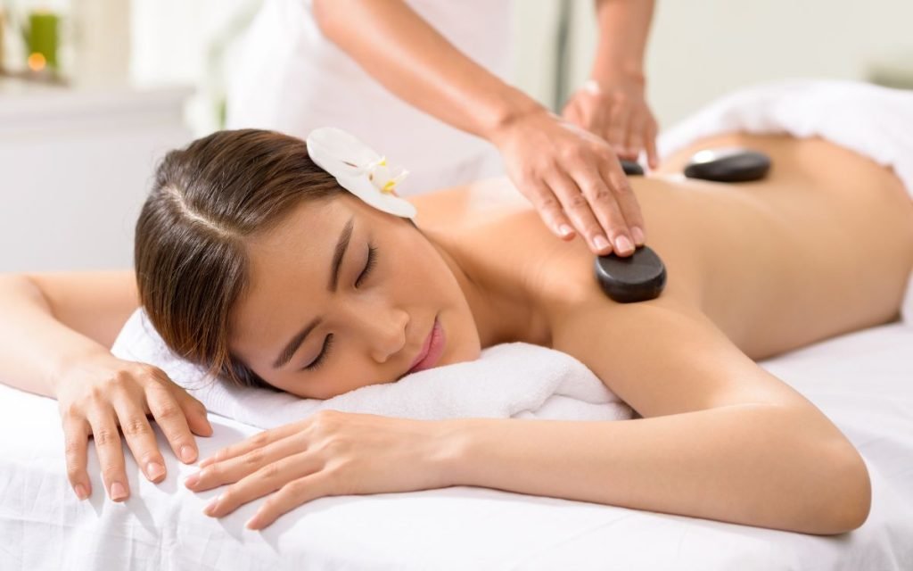 Người đang nằm thư giãn trên giường massage, được trị liệu bằng đá nóng trên lưng, trong không gian spa yên tĩnh.