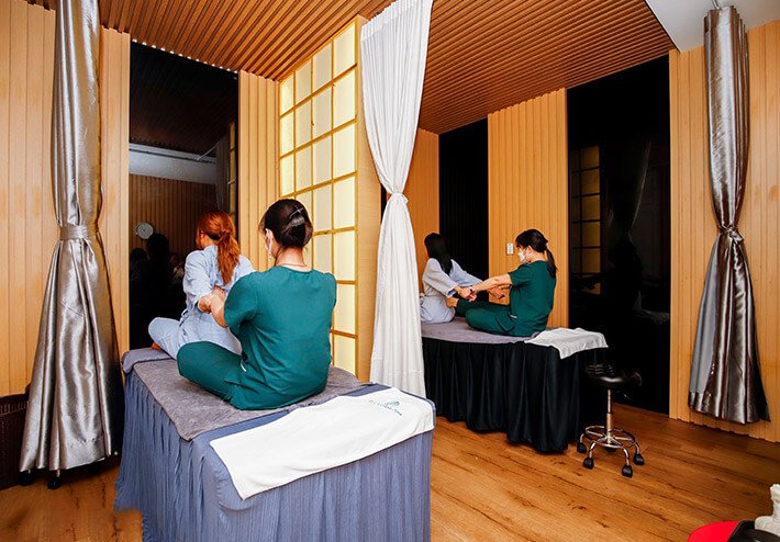 Phòng massage với hai khách hàng đang được nhân viên thực hiện liệu pháp thư giãn trên giường massage.