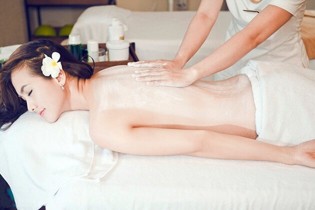 Người đang nằm thư giãn trên giường massage, được thoa kem và massage lưng bởi một chuyên viên.
