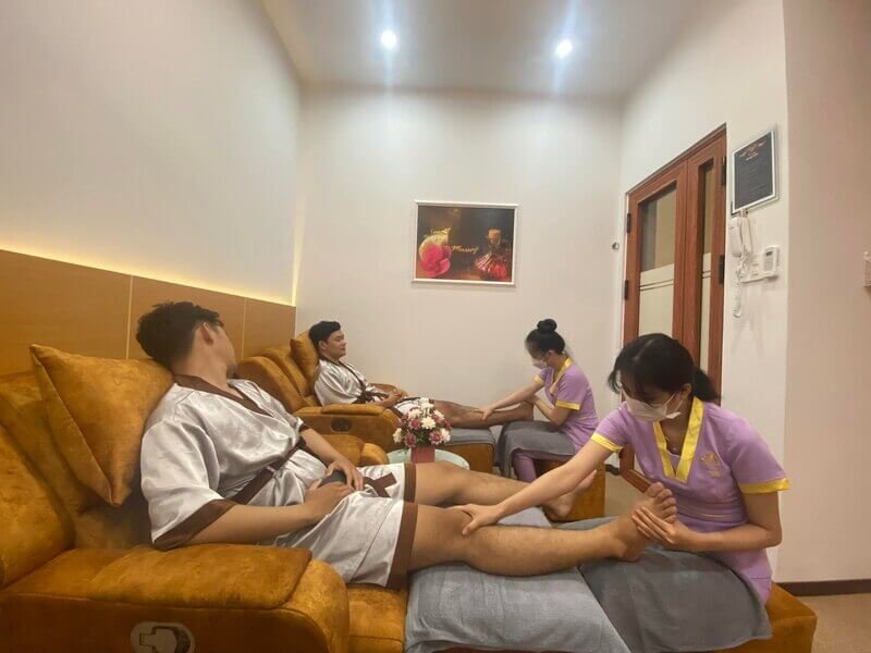 Hai khách hàng trong phòng spa được nhân viên chăm sóc chân, không gian ấm cúng với tranh treo tường.