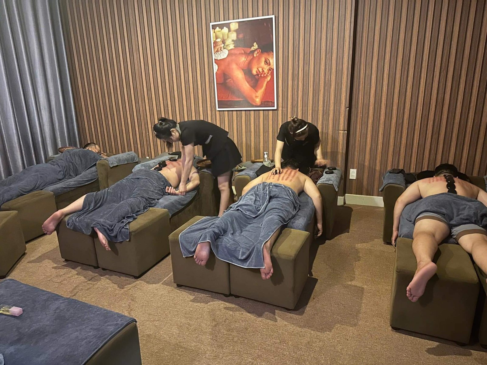 Những người đang được massage trong một phòng có tường gỗ, với tranh treo trên tường.