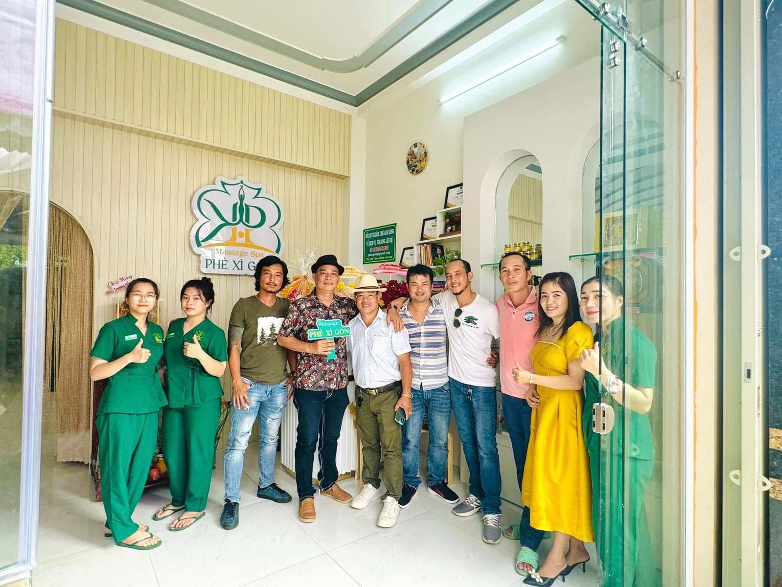 Nhóm người đứng trong không gian spa, cùng tạo dáng chụp ảnh, phía sau có bảng hiệu và kệ trưng bày.