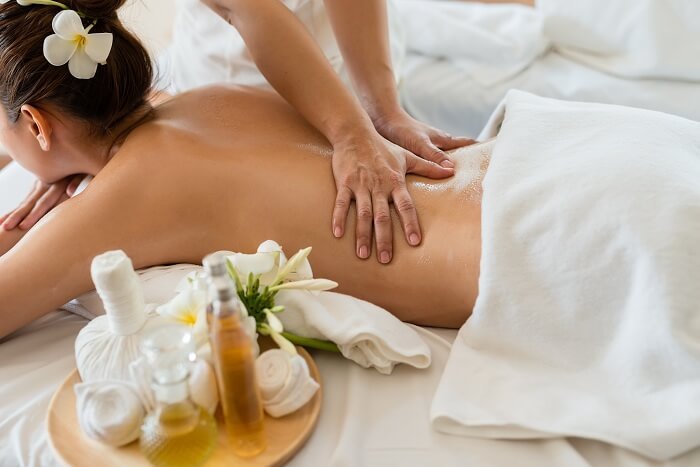 Người đang được massage lưng trong không gian thư giãn với khăn trắng và dầu massage, hoa trang trí bên cạnh.