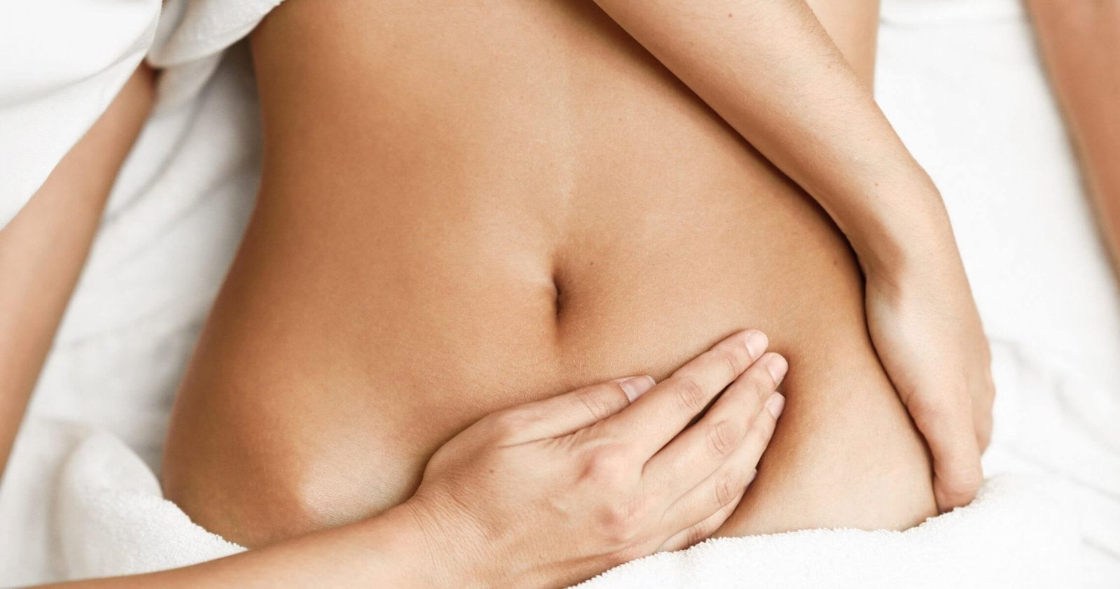 Người đang được massage bụng, tay đặt nhẹ nhàng trên da, trên nền vải trắng.