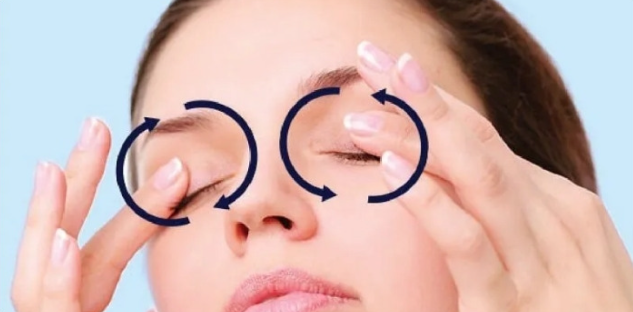 Người đang thực hiện massage vùng mắt với các mũi tên chỉ hướng chuyển động tròn.