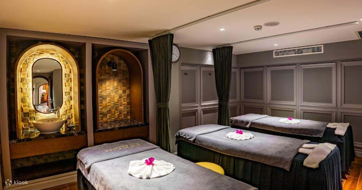 Phòng spa với ba giường massage, trang trí bằng đá và ánh sáng vàng dịu, tạo không gian thư giãn.