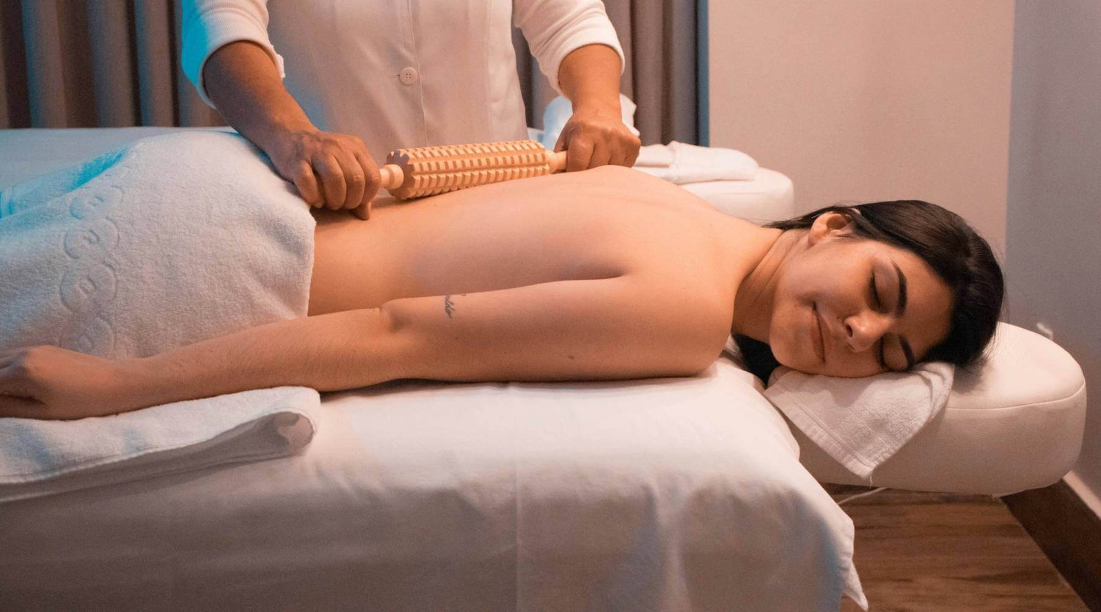 Người nằm trên giường massage, được áp dụng liệu pháp với dụng cụ gỗ, trong không gian spa thoải mái.